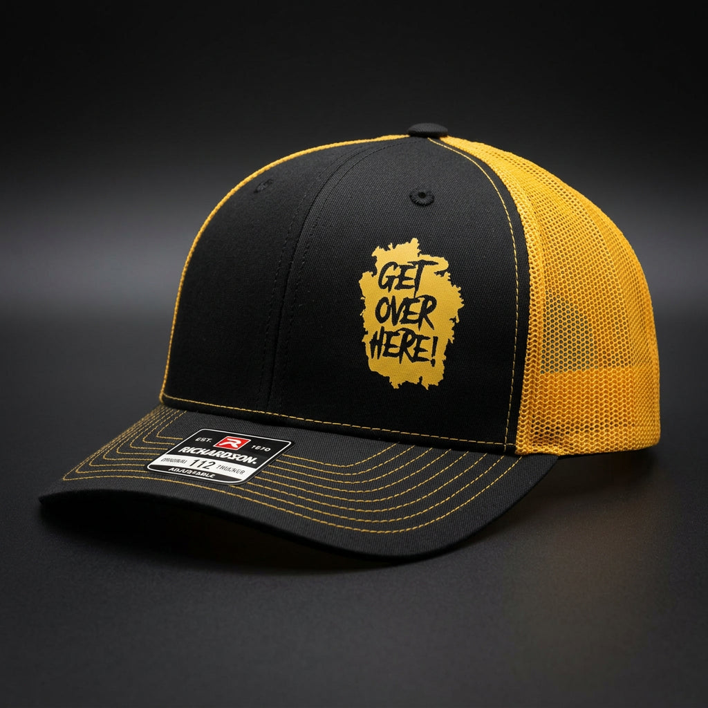 "Get Over Here!" black and gold trucker hat, three-quarter view showing gold mesh side